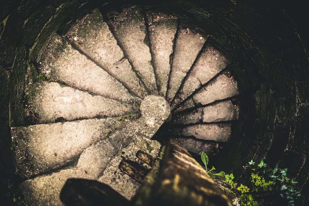 A worn stone spiral staircase in a castle seen from directly above, its wedge-shaped treads turning around the central newel post.