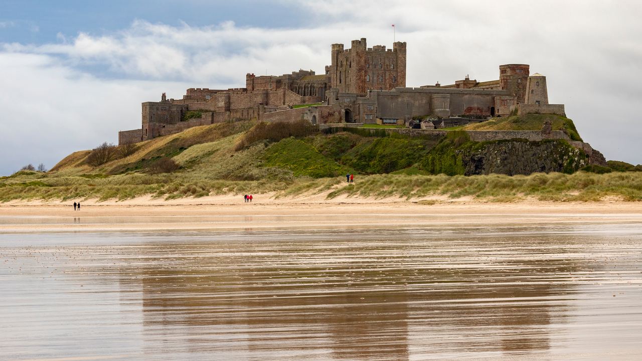 Bamburgh Castle standing on its dune ridge above the wide tidal sands of the Northumberland coast in England.