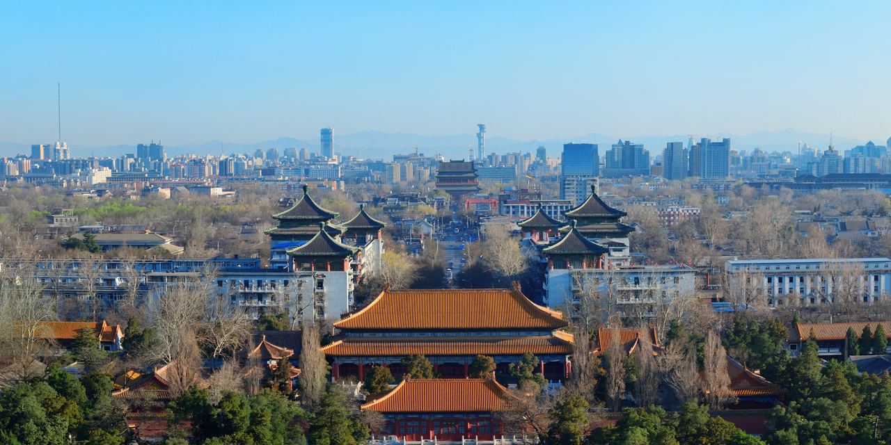 The tiled roofs and painted eaves of old Beijing in the foreground, with the towers of the modern city rising behind them.