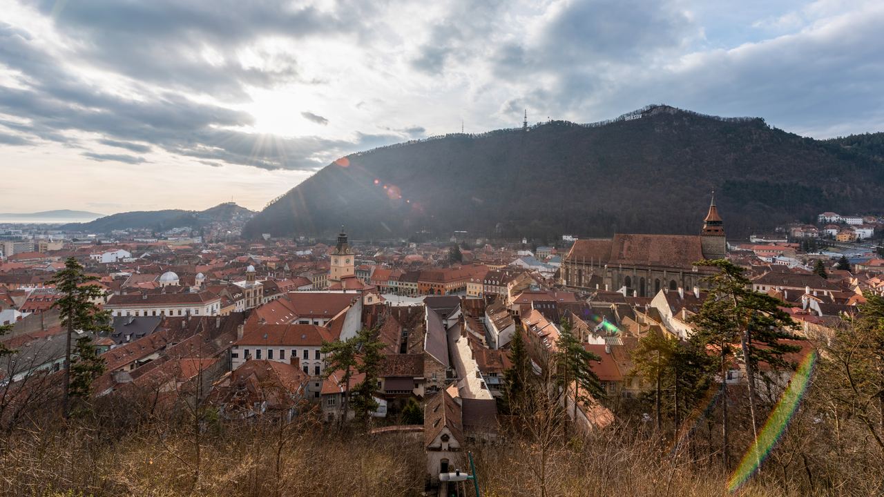 The red roofs of the old town of Brasov spread beneath the wooded bulk of Mount Tampa under a heavy sky.
