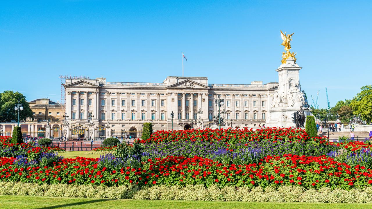 The east front of Buckingham Palace behind beds of red flowers, with the gilded Victoria Memorial on the right.