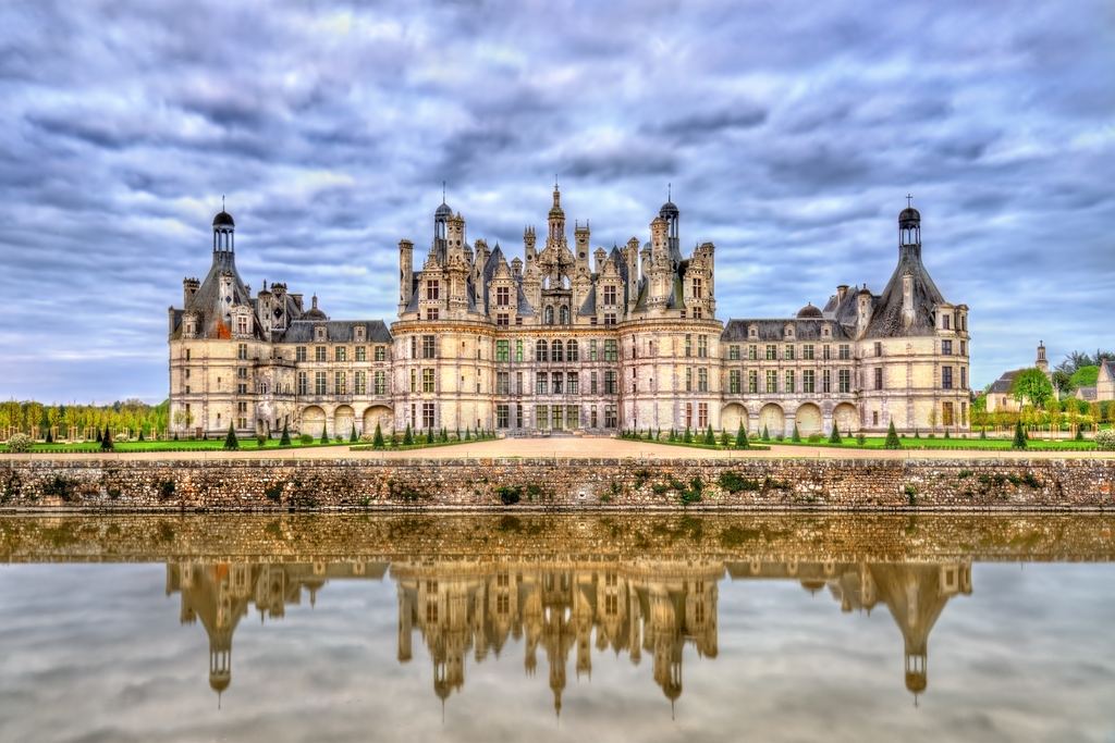 The full north front of the Chateau de Chambord and its roofline of towers reflected in the canal.