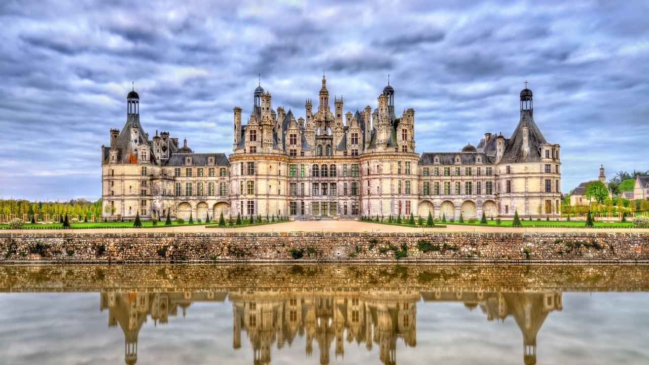 The full north front of the Chateau de Chambord and its roofline of towers reflected in the canal.