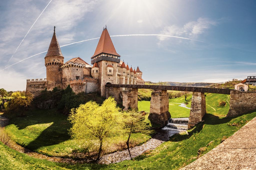 The red-roofed towers of Corvin Castle in Hunedoara with the long wooden bridge running to its gate over the green ravine.