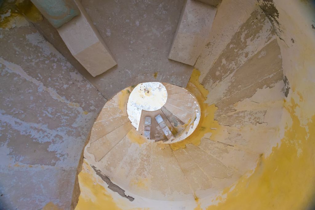 Looking down the narrow stone spiral staircase of a fortress tower, the treads worn and the central newel post rising through the middle.