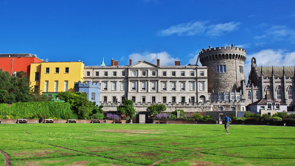 The Record Tower and state apartments of Dublin Castle seen across the lawn, with coloured Georgian houses to one side.