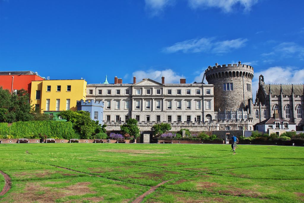 The Record Tower and state apartments of Dublin Castle seen across the lawn, with coloured Georgian houses to one side.