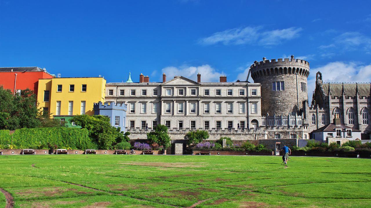 The Record Tower and state apartments of Dublin Castle seen across the lawn, with coloured Georgian houses to one side.