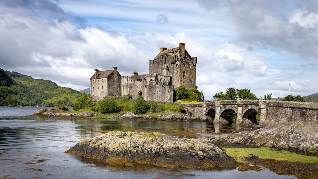 The arched stone bridge leading to Eilean Donan Castle under a heavy Highland sky.