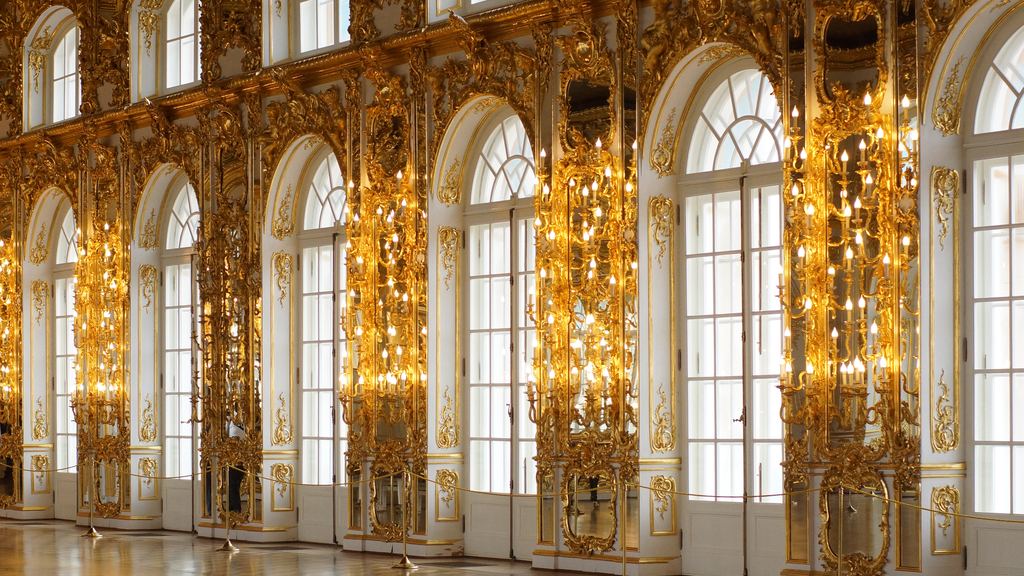 Gilded pilasters and tall arched windows along one side of the Hall of Mirrors at Versailles.