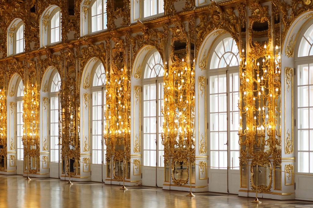 Gilded pilasters and tall arched windows along one side of the Hall of Mirrors at Versailles.