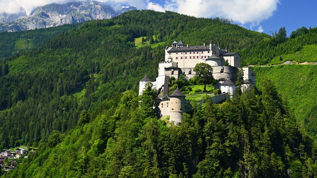 Hohenwerfen Castle standing white on its steep green knoll in the Salzach valley, with alpine slopes rising behind.