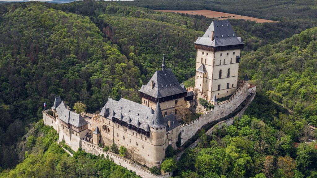 Karlstejn Castle stepping down its wooded ridge in Bohemia, the Great Tower at the top above the lower palace and walls.