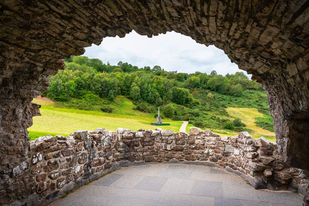 A broken stone arch at Urquhart Castle framing the green banks of Loch Ness, with nothing but grass and sky where rooms once stood.
