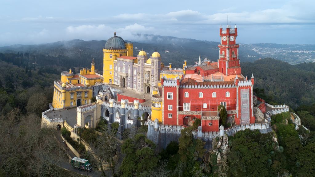 The Pena National Palace at Sintra in the morning, its yellow and red wings standing above the wooded hills.
