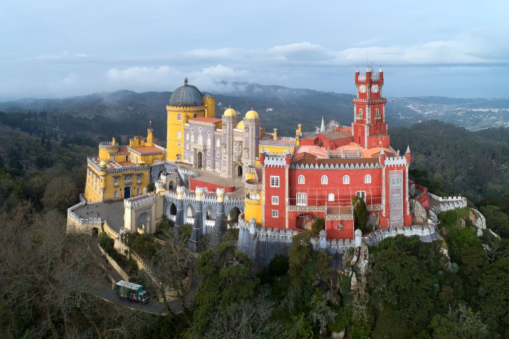 The Pena National Palace at Sintra in the morning, its yellow and red wings standing above the wooded hills.