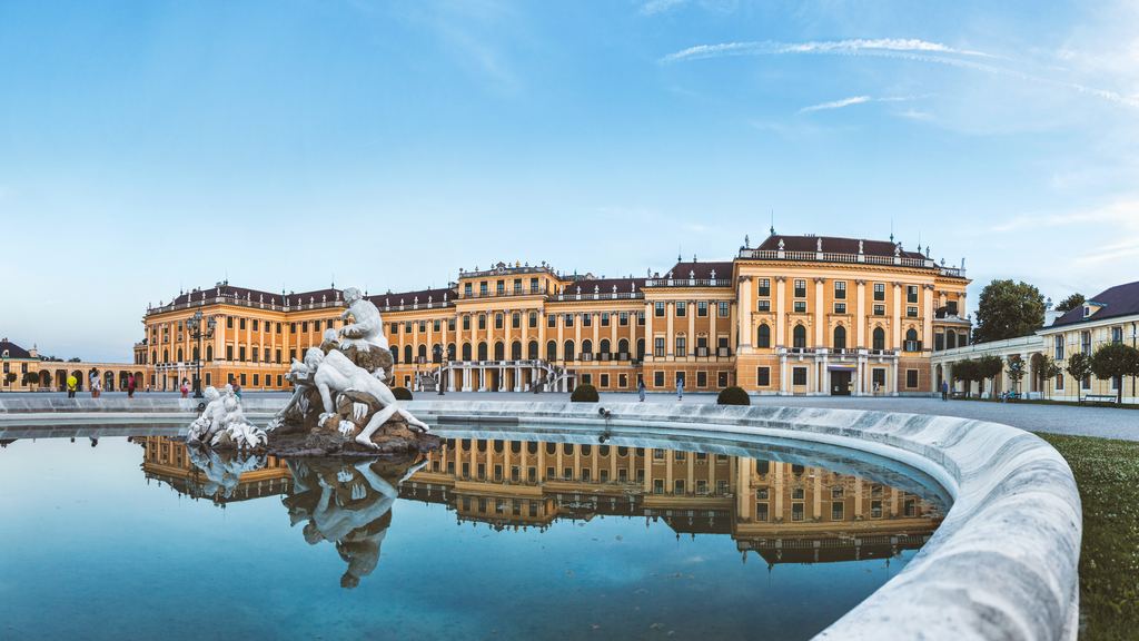 The ochre facade of Schoenbrunn Palace reflected in the still water of the fountain basin in its Vienna gardens.