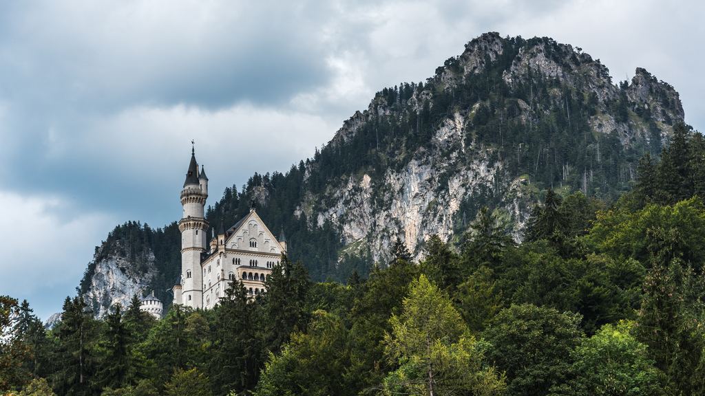 The wooded rock walls of the Bavarian Alps above Hohenschwangau, with Neuschwanstein small on the ridge under the cliffs.