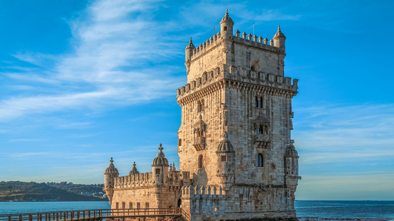The Belem Tower standing at the edge of the Tagus in Lisbon, its stone gallery and turrets against a clear sky.