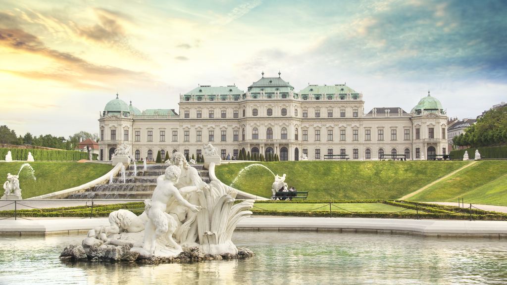 The Upper Belvedere in Vienna in warm evening light, seen behind the carved stone figures of the garden fountain.