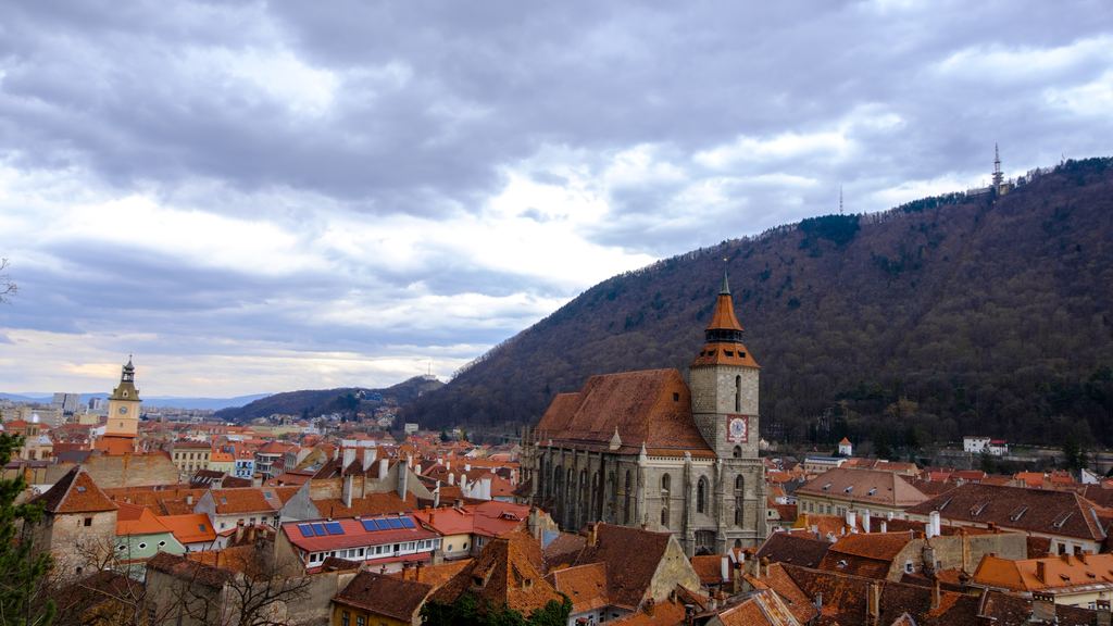 The tower of the Black Church rising over the red roofs of Brasov, with the forested slope of Mount Tampa behind.