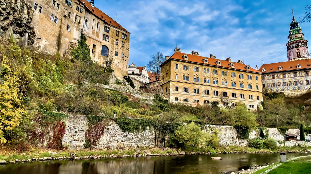 The painted walls and terraces of Cesky Krumlov castle standing on the rock above the green water of the Vltava.