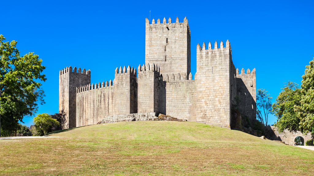 The keep and curtain wall of the castle of Guimaraes rising from its grassy mound under a clear blue sky.
