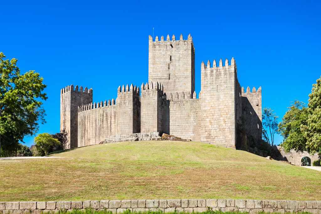 The keep and curtain wall of the castle of Guimaraes rising from its grassy mound under a clear blue sky.
