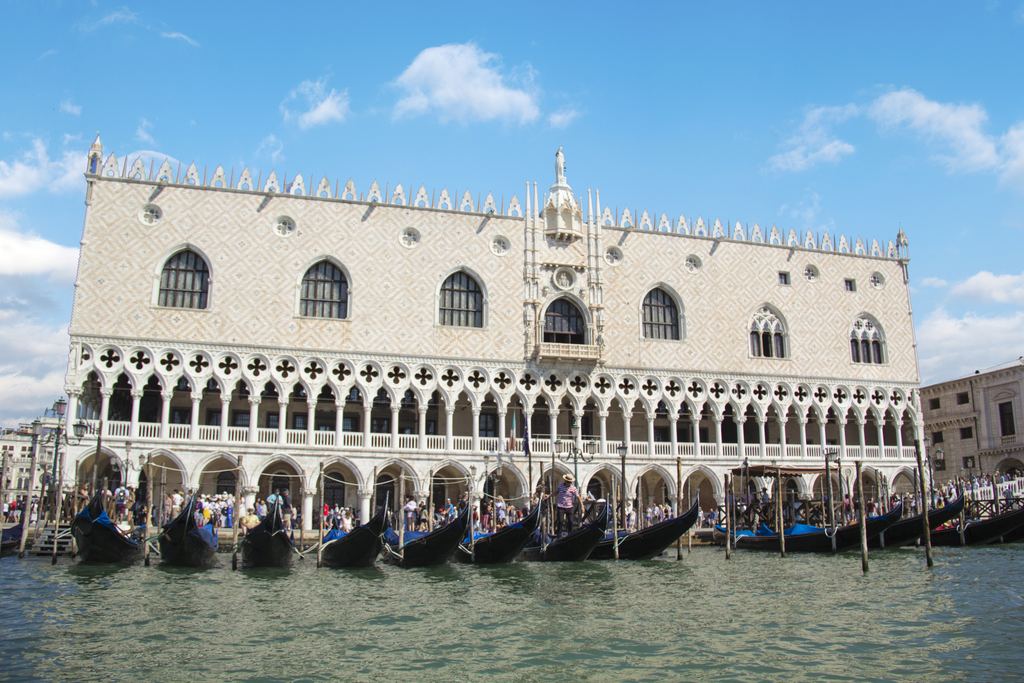 The full pink and white front of the Doge's Palace along the Venetian waterfront, with gondolas moored in front of it.