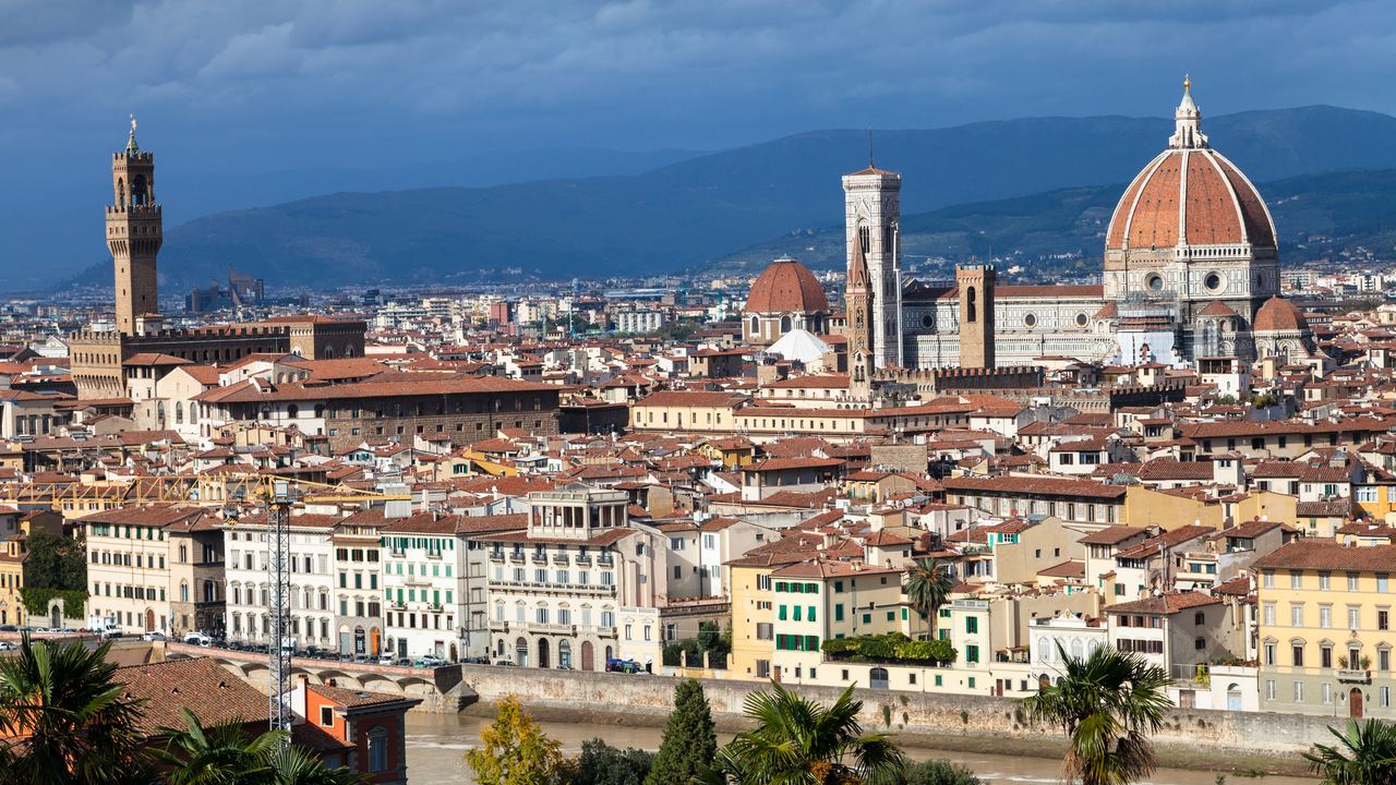 The Florence skyline seen from above, the dome of the cathedral and the tower of Palazzo Vecchio rising over the tiled roofs of the old city.