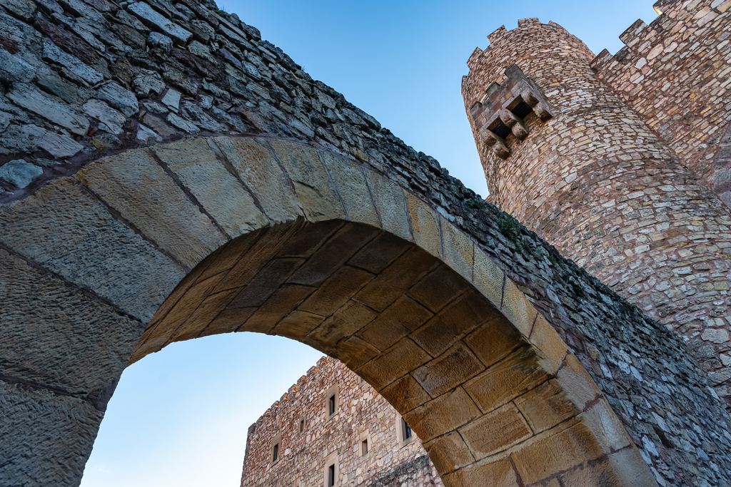 The arched stone gateway of the castle of Sigüenza seen from below, with a battlemented drum tower rising beside it.