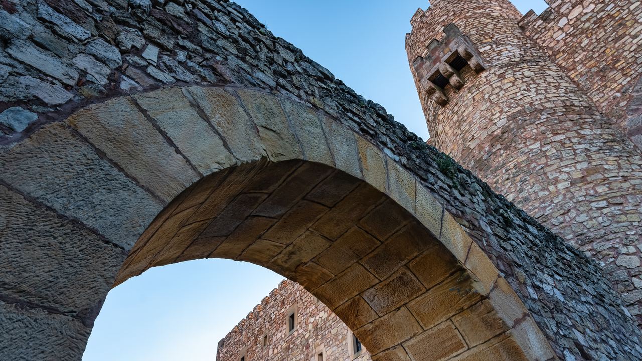 The arched stone gateway of the castle of Sigüenza seen from below, with a battlemented drum tower rising beside it.