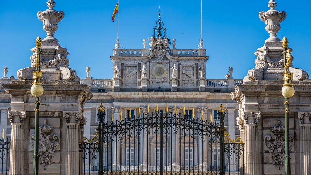 The gilded ironwork gates in front of the Royal Palace of Madrid against a clear sky.