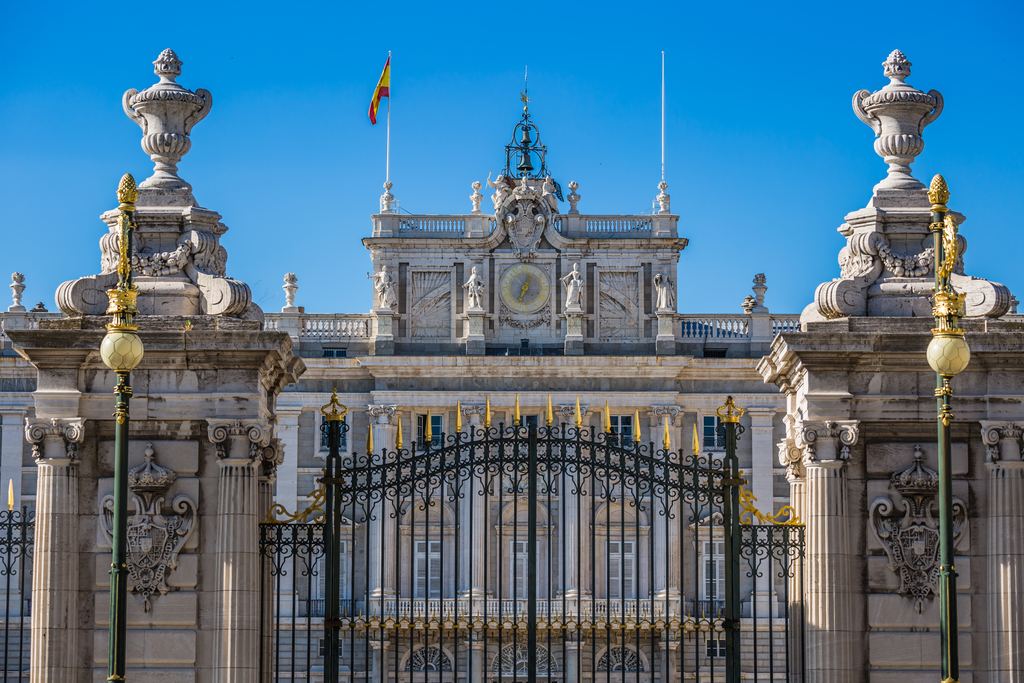 The gilded ironwork gates in front of the Royal Palace of Madrid against a clear sky.