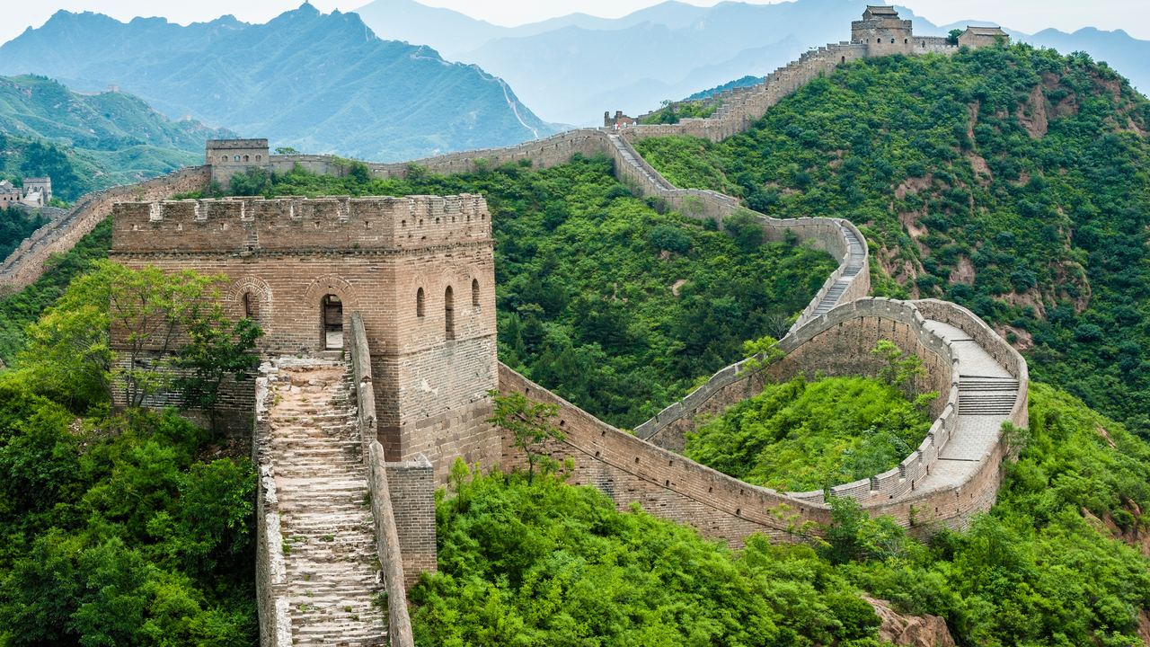 The Great Wall running along the crest of green ridges at Jinshanling, its watchtowers stepping away into the haze.