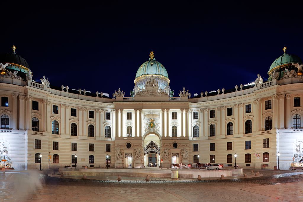 The curved wing and green dome of the Hofburg palace lit at night above Michaelerplatz in the centre of Vienna.