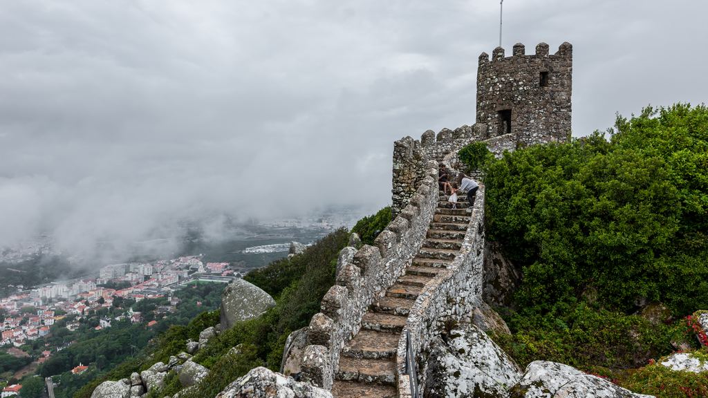 The wall of the Castelo dos Mouros running along its rocky ridge above Sintra, its watchtower standing in drifting fog.