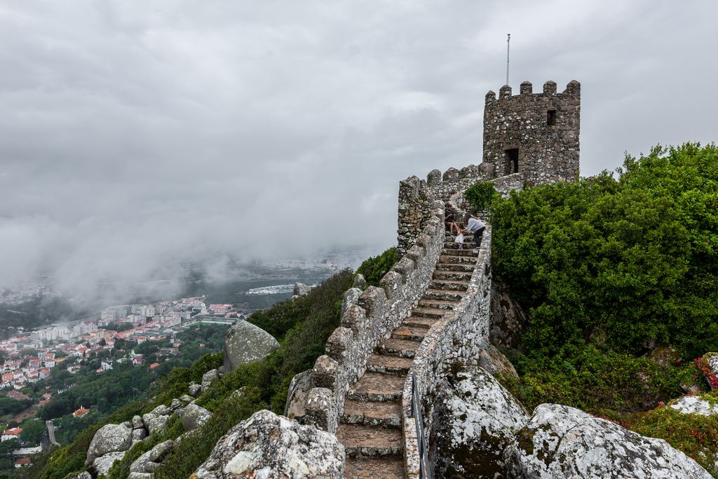 The wall of the Castelo dos Mouros running along its rocky ridge above Sintra, its watchtower standing in drifting fog.