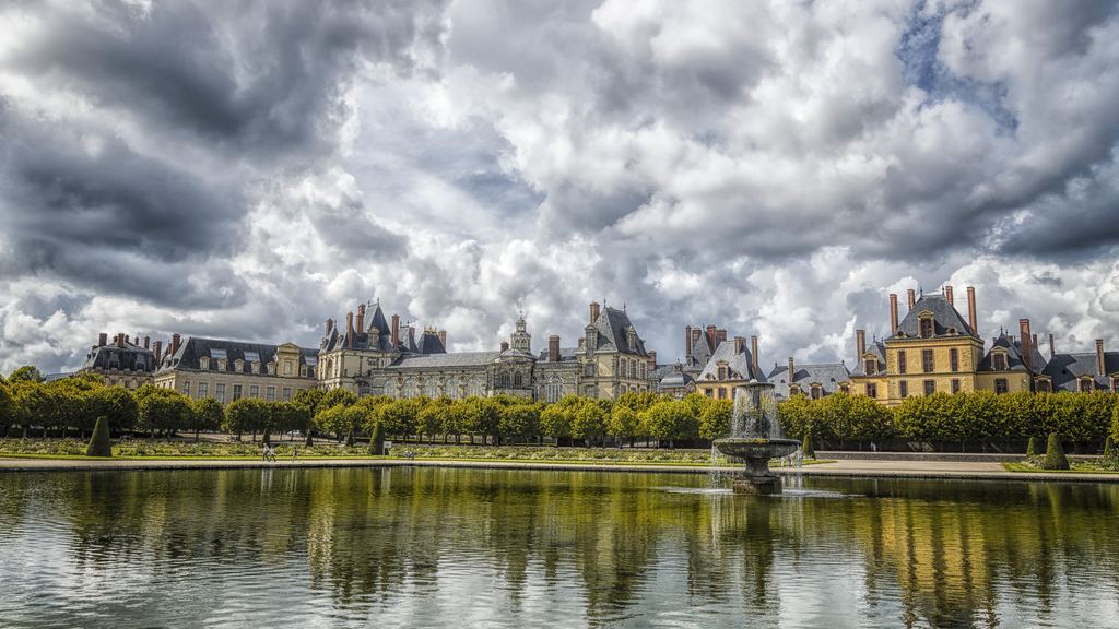 The long front of the Palace of Fontainebleau seen across the carp pond under a heavy sky.
