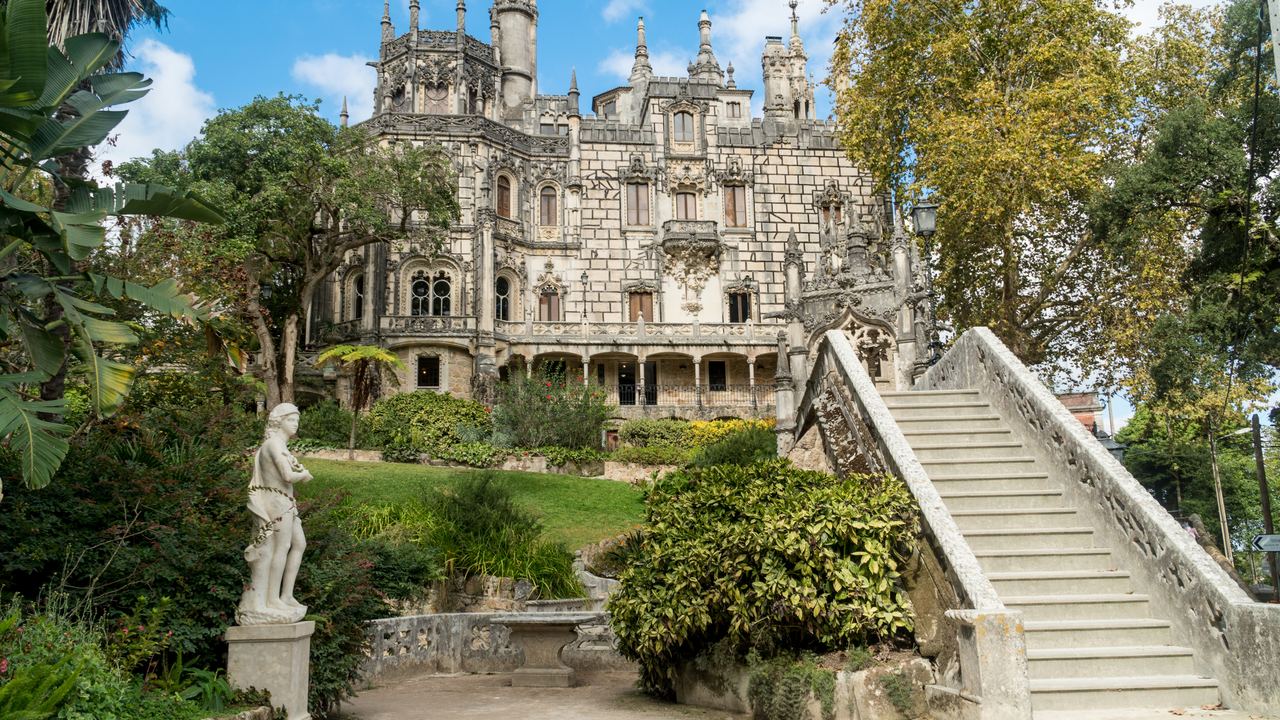 The Regaleira palace at Sintra behind its garden staircase and statue, framed by the autumn trees of the estate.