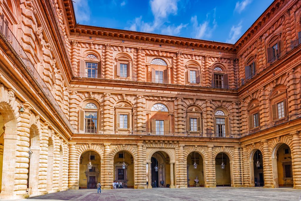 The heavy rusticated stone of the Ammannati courtyard at Palazzo Pitti, its warm orange walls rising under a blue sky.