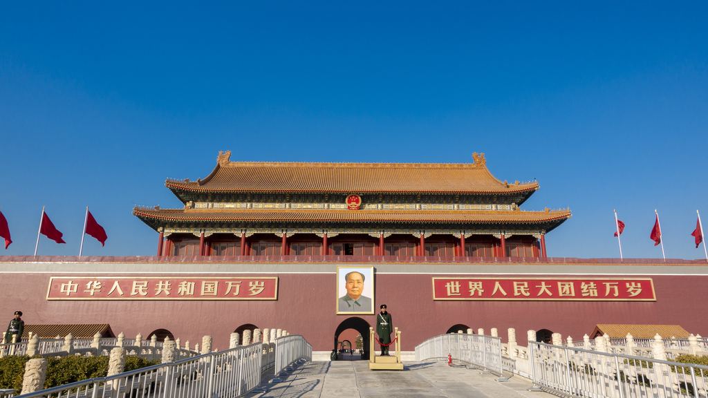 The Tiananmen gate in Beijing, its red wall, tiled roof and red flags standing against a deep blue sky.