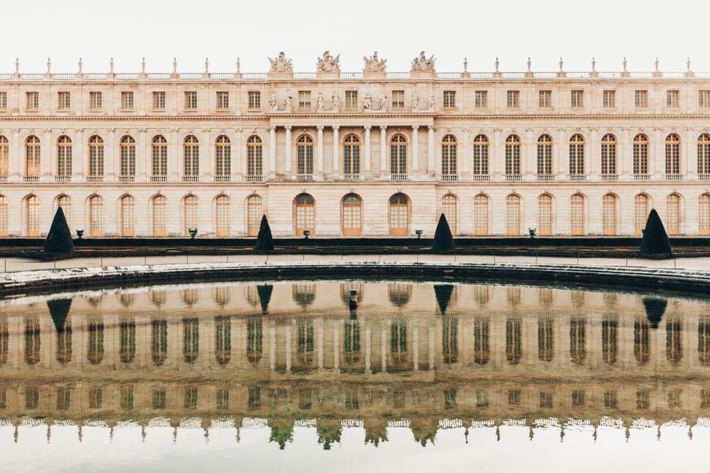 The long garden facade of the Palace of Versailles reflected in the still water in front of it.