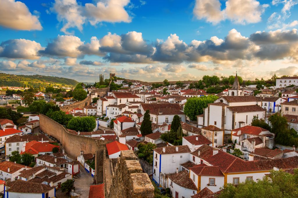 The walled town of Obidos seen from its ramparts, white houses and red roofs spread beneath a wide bank of cloud.