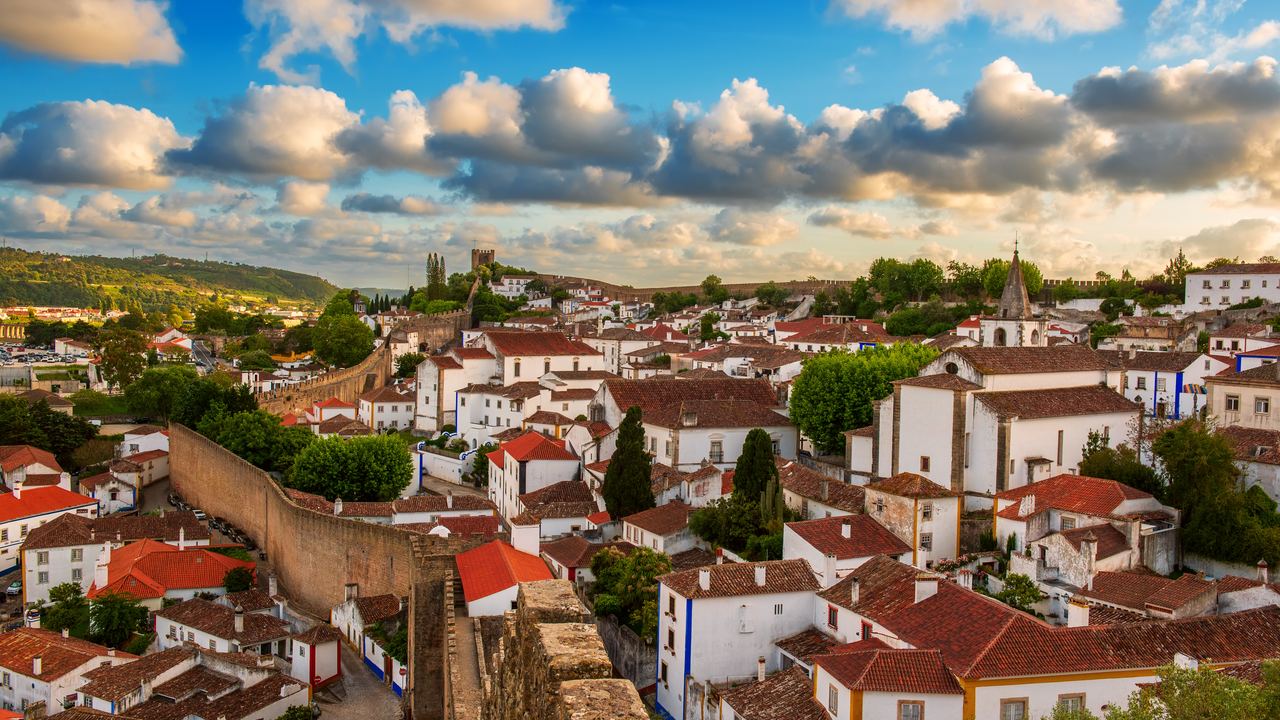 The walled town of Obidos seen from its ramparts, white houses and red roofs spread beneath a wide bank of cloud.