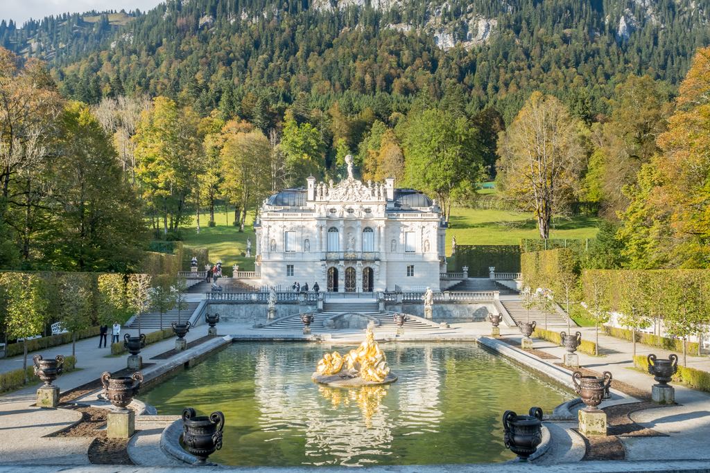 The front of Linderhof Palace reflected in its fountain basin, with the gilded figures of the water parterre in front.